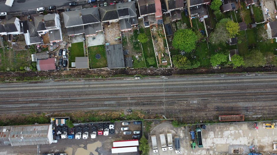 This aerial image captures a row of residential houses with varied roof styles, including tiled and flat roofs made of materials like slate and asphalt, along with small backyards and garden areas. Th