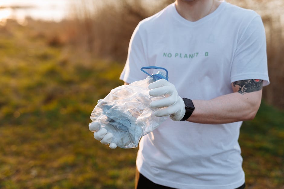 A person wearing white sneakers, black shorts, and a light blue T-shirt is using a litter picker to collect waste from a large pile of dark grey and brown rocks with rough textures, some with patches 